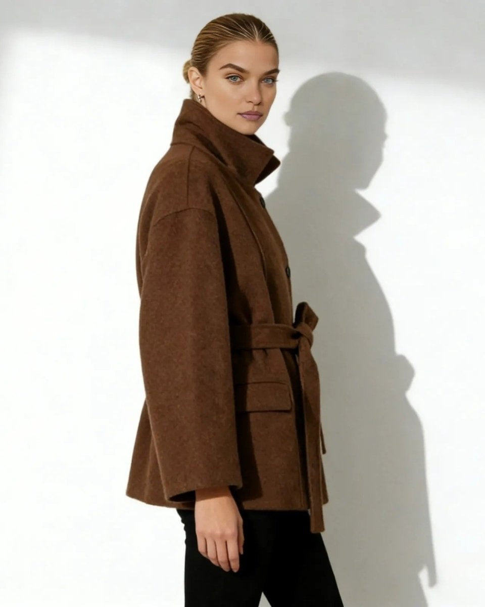 Side profile of a model in the brown wool jacket showing the sculptural high collar and sleeve shape.