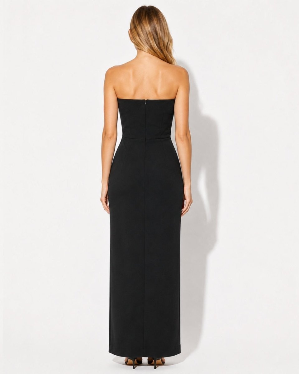 A woman viewed from the back wearing a strapless black maxi dress against a plain white studio background.