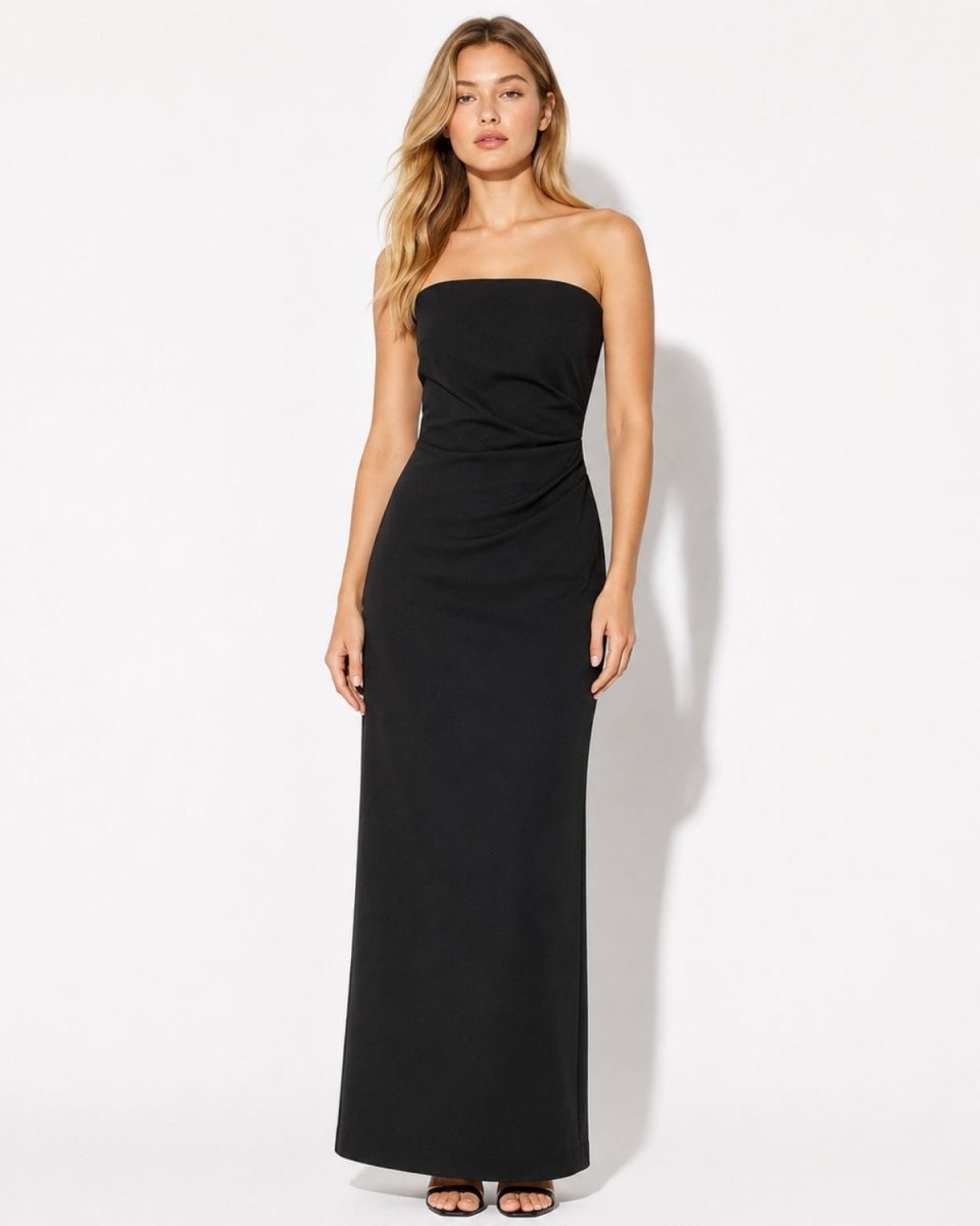 A woman modeling a strapless black maxi dress with a ruched waist, standing against a plain white studio background.