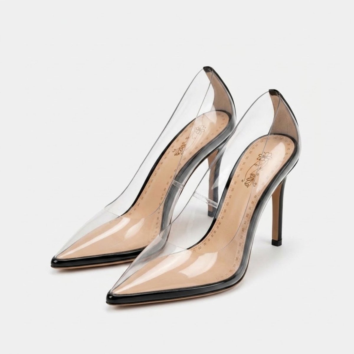 A pair of clear patent leather pointed-toe pumps with slim stiletto heels, shown on a light gray background.