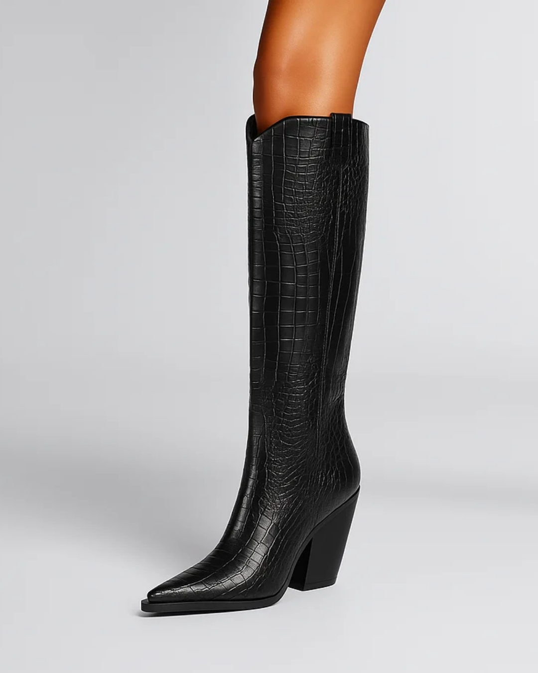 A black knee-high boot with an embossed crocodile pattern, featuring a pointed toe and a chunky block heel, shown on a model's leg against a light gray background.