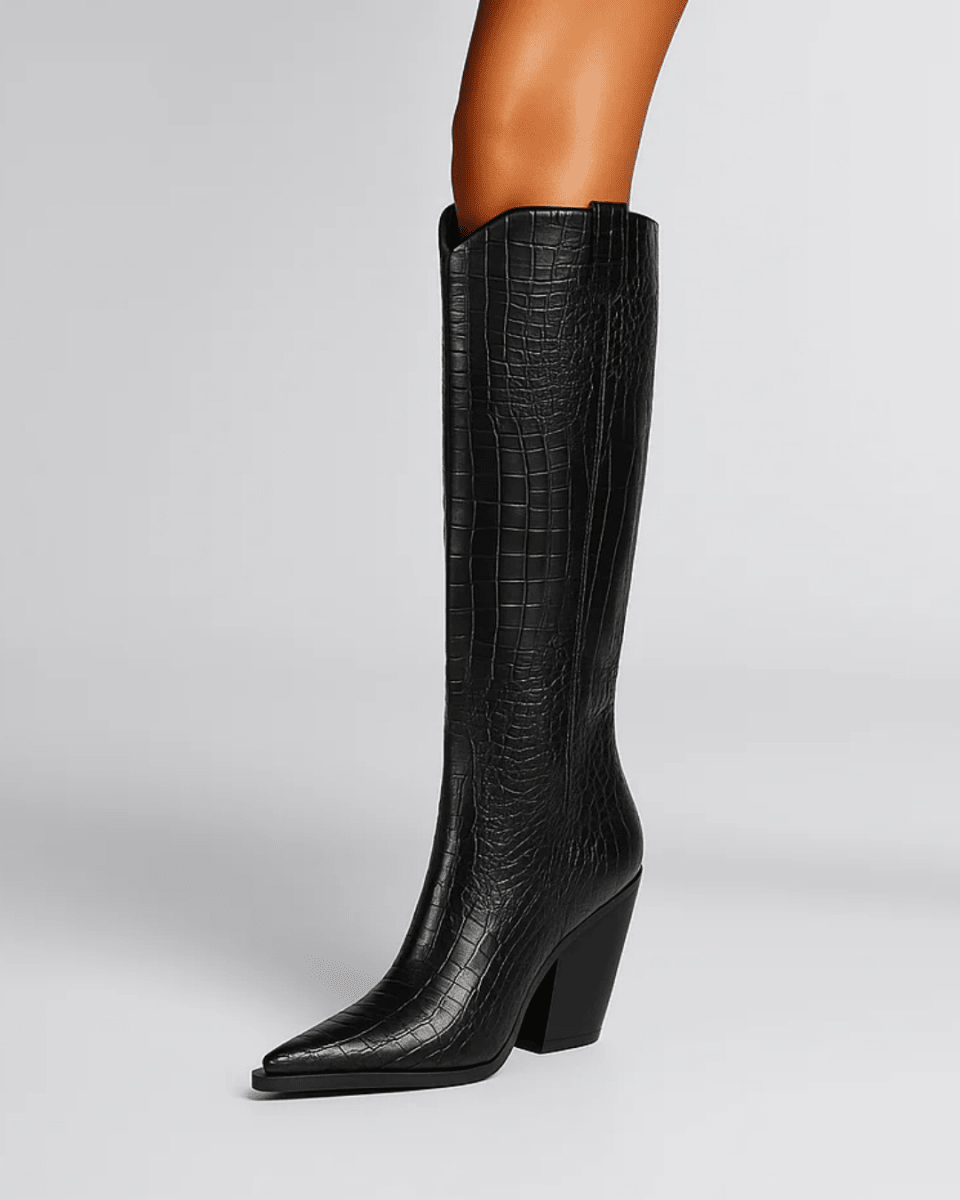 A black knee-high boot with an embossed crocodile pattern, featuring a pointed toe and a chunky block heel, shown on a model's leg against a light gray background.