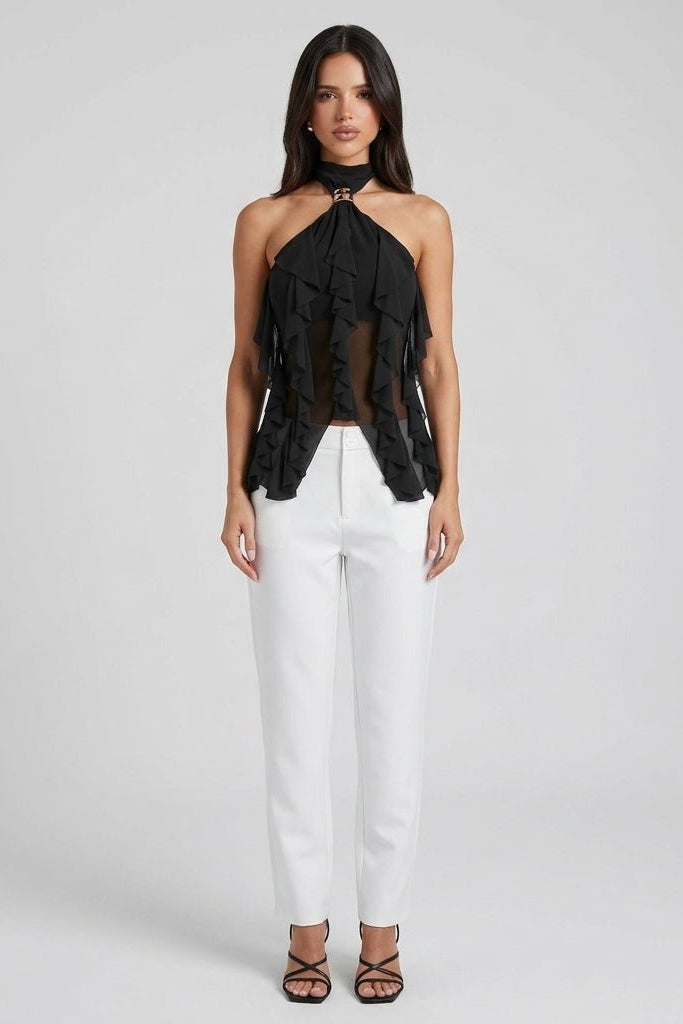 Full body front view of woman modeling the Fenlo Form black cascading ruffle party top with high-waisted white trousers on a seamless grey background.