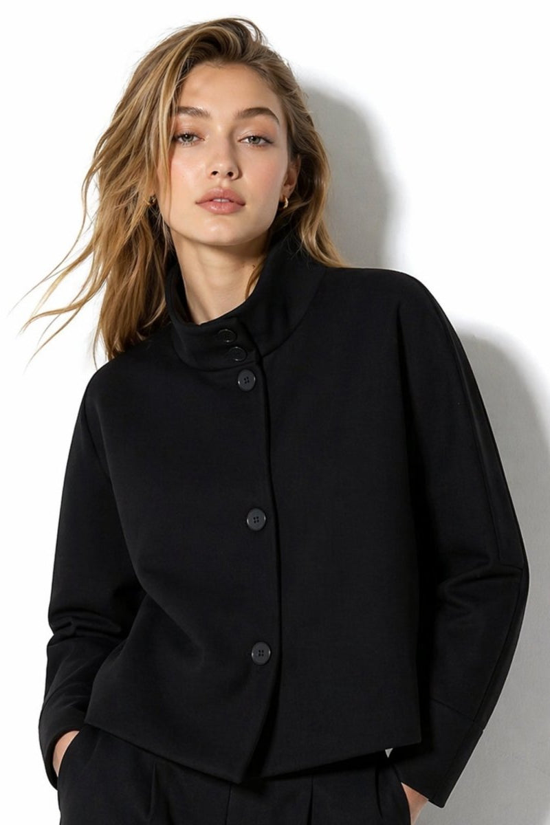 Woman wearing  Fenlo Form black funnel neck structured cropped jacket with asymmetrical buttons.