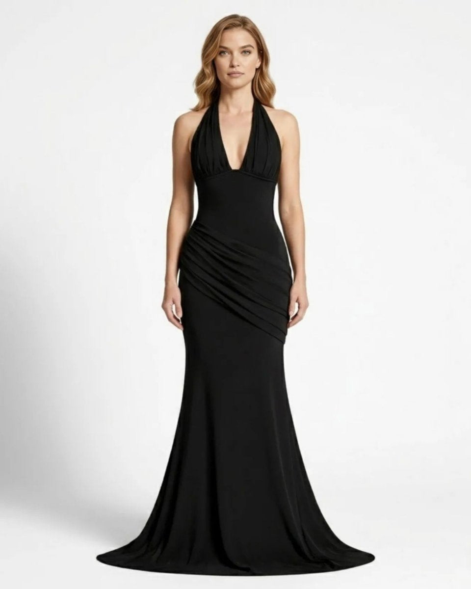 Elegant blonde woman wearing a Fenlo black halter neck corset maxi dress with ruched waist details, standing front facing against a white studio background.