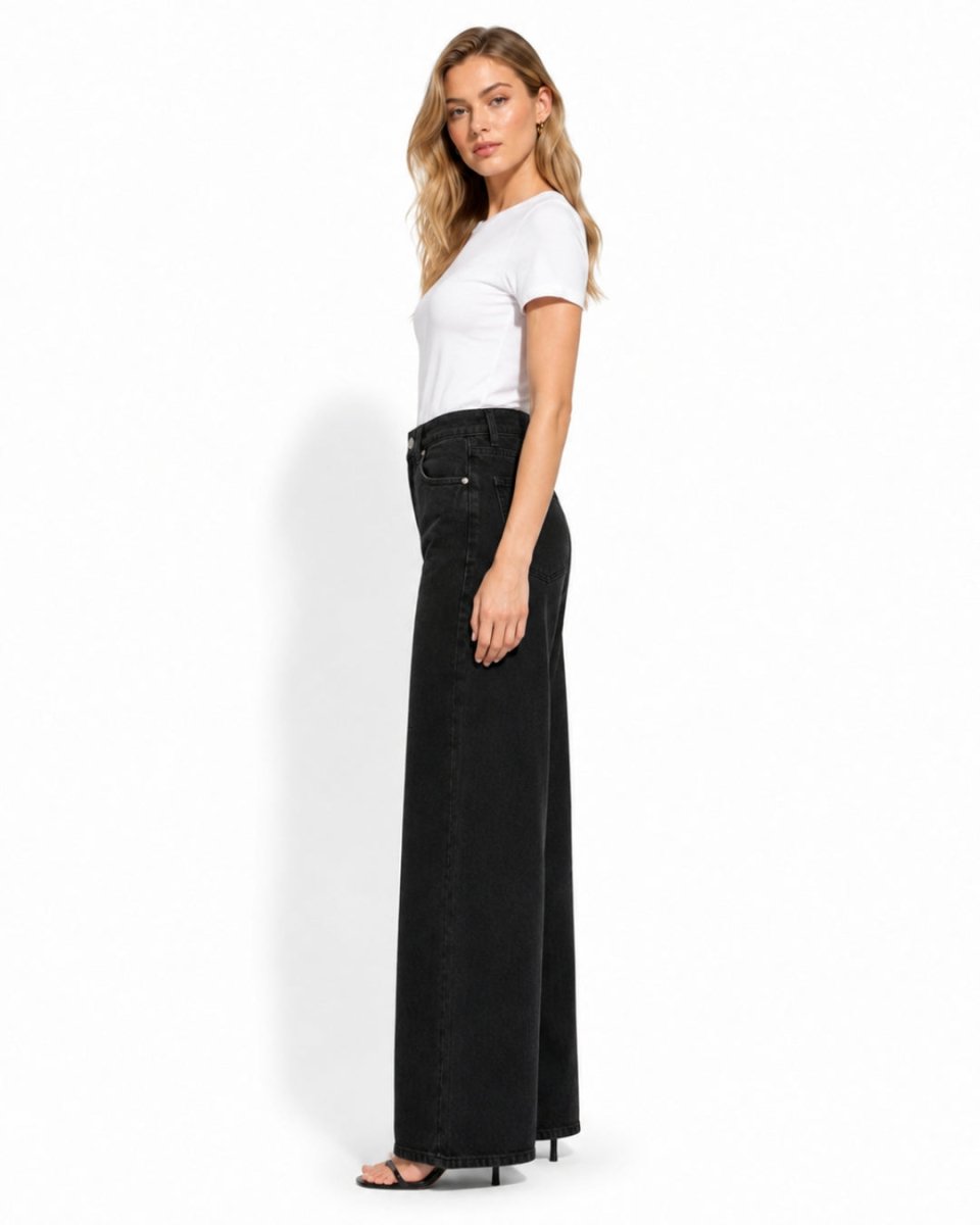 A woman modeling a pair of black wide-leg denim pants with a white t-shirt, standing against a plain white studio background.