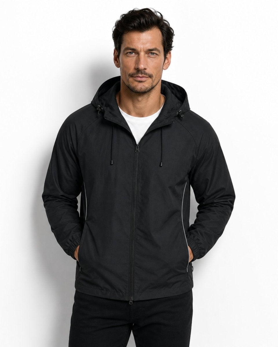 Man modeling black water-resistant athletic jacket with hood down and hands in pockets.