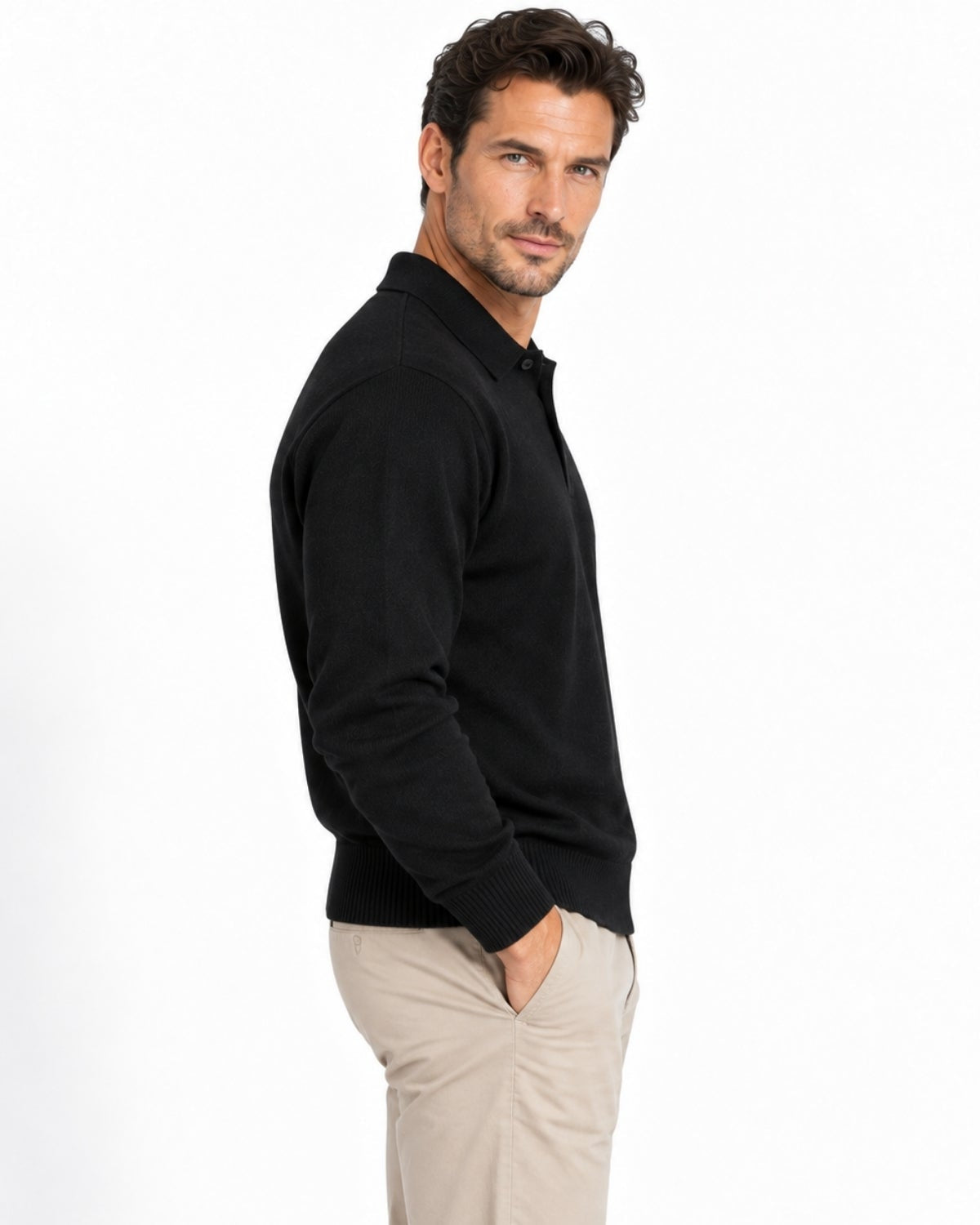 A man wearing a black long-sleeve knit polo shirt and beige trousers, shown in profile against a plain white studio background.