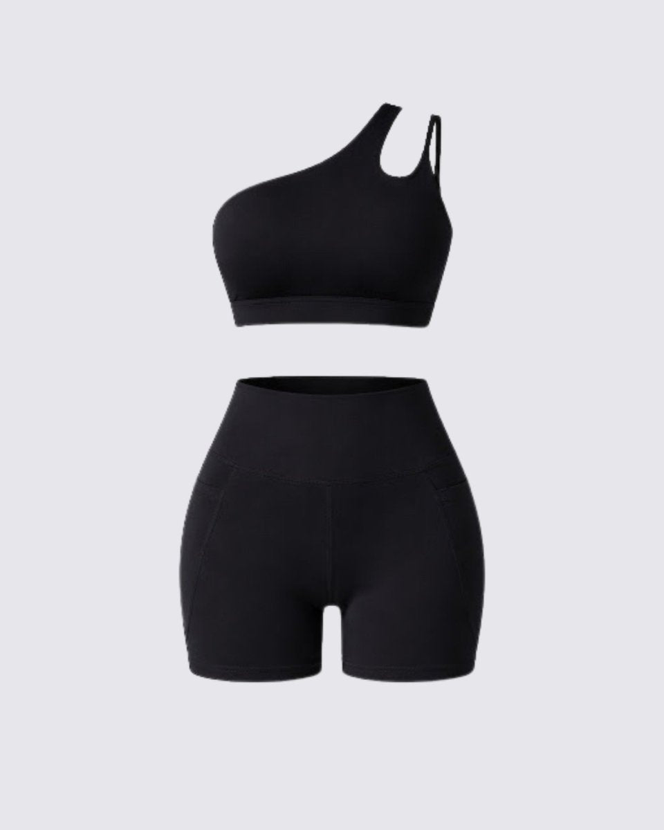 Flat lay of black luxury activewear set showing one shoulder sports bra with cutout and high waisted pocket biker shorts