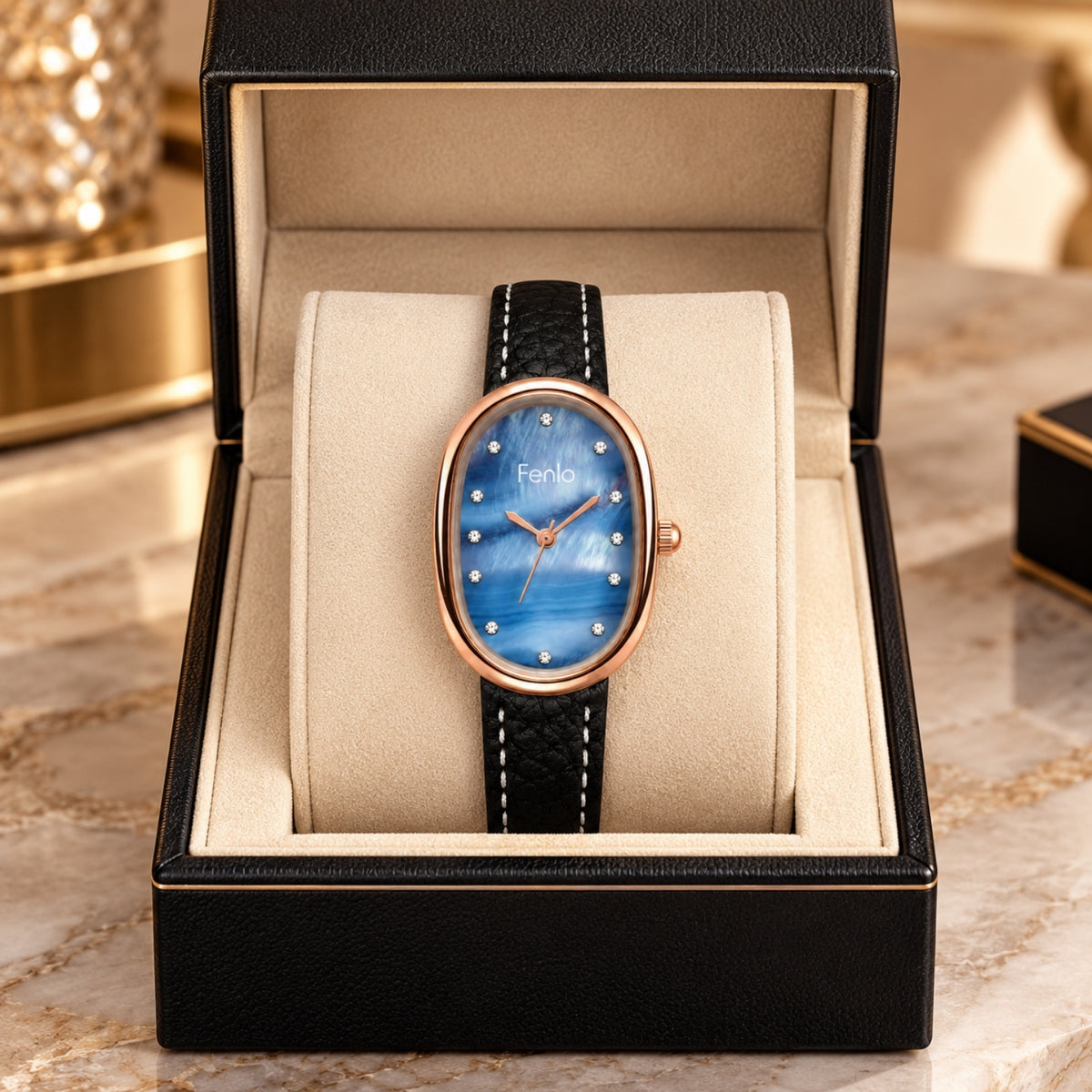 A Ferla wristwatch with an oval blue dial and black textured strap, presented inside an open black luxury gift box with a beige interior on a marble surface.