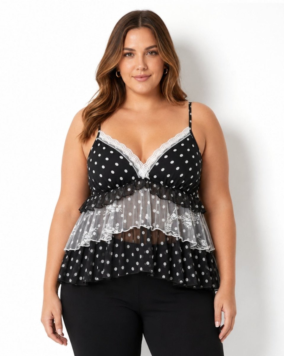 A woman modeling a black camisole top with white polka dots, featuring a sheer white mesh ruffle panel across the midsection and white lace trim at the neckline, paired with black pants against a plain white background.