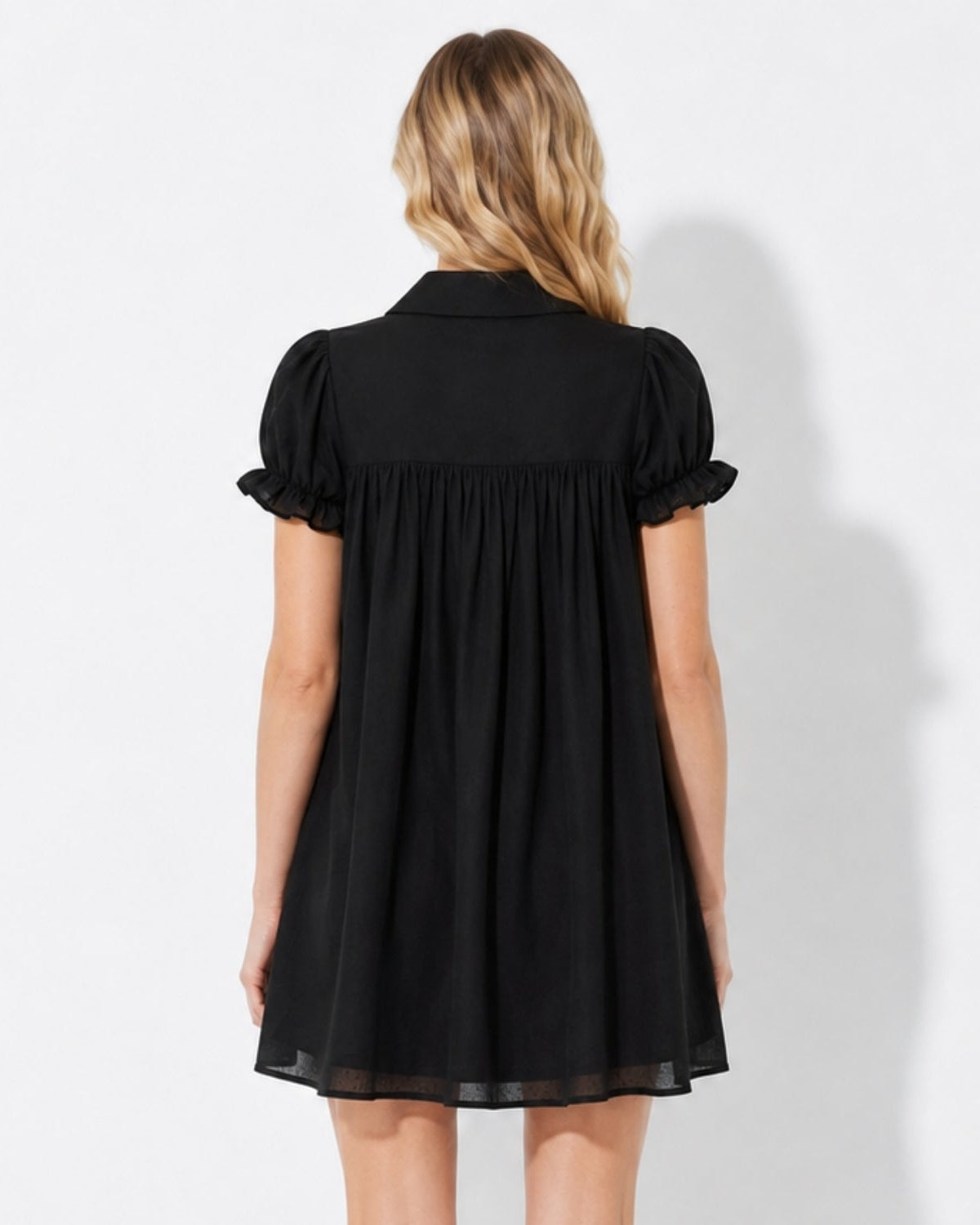Back view of the black luxury coquette mini dress highlighting the elegant gathered empire waistline and crisp structured collar.