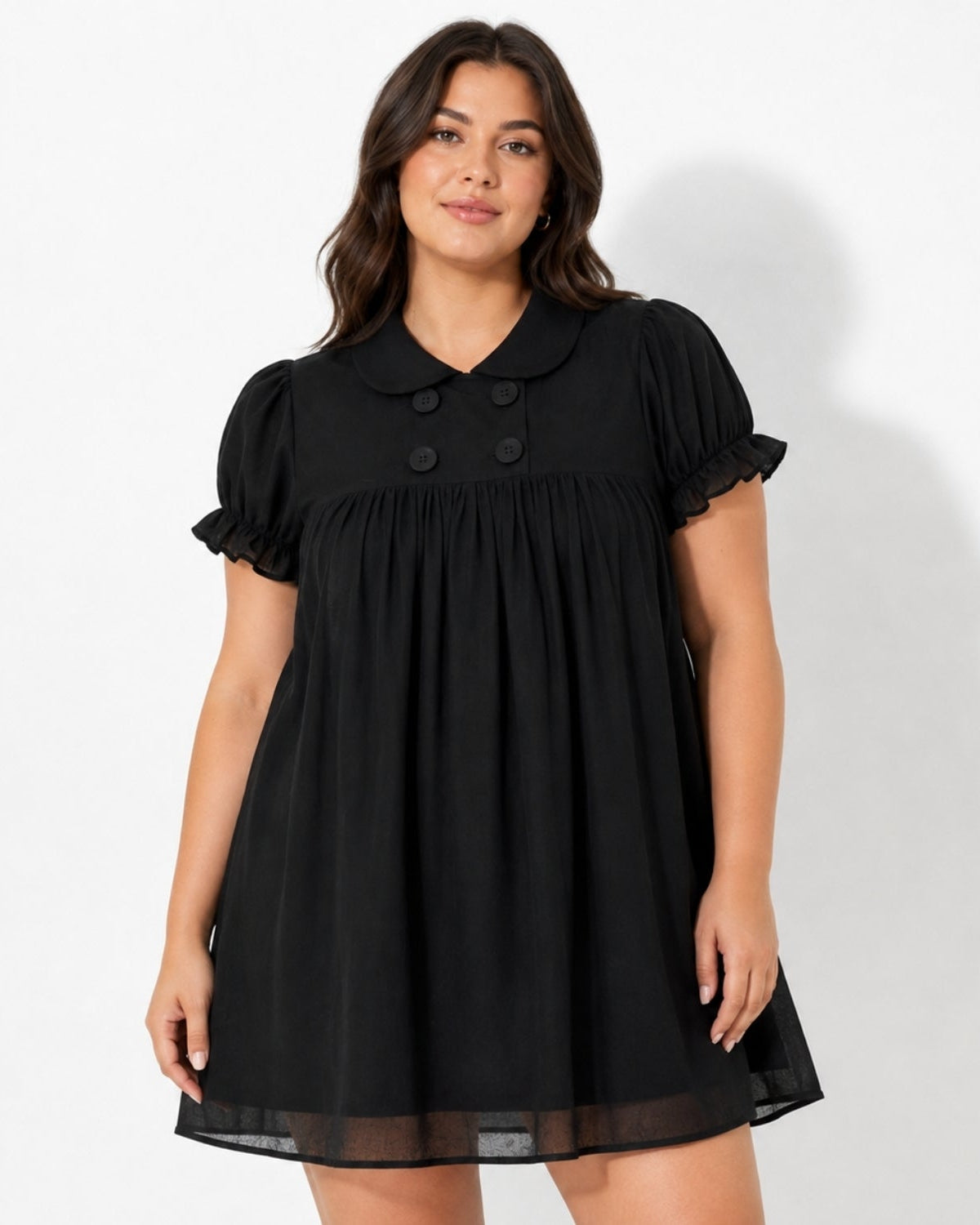 A woman modeling a black short-sleeve babydoll dress with a Peter Pan collar, double-breasted buttons, and ruffled sleeves against a white studio background.