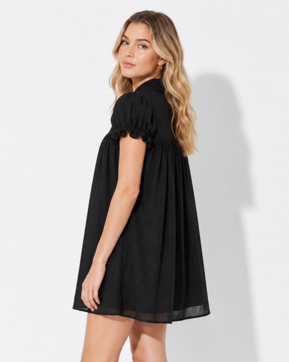 Side profile of a model wearing a voluminous black smock mini dress featuring ruffled short puff sleeves and a flowing A-line silhouette.