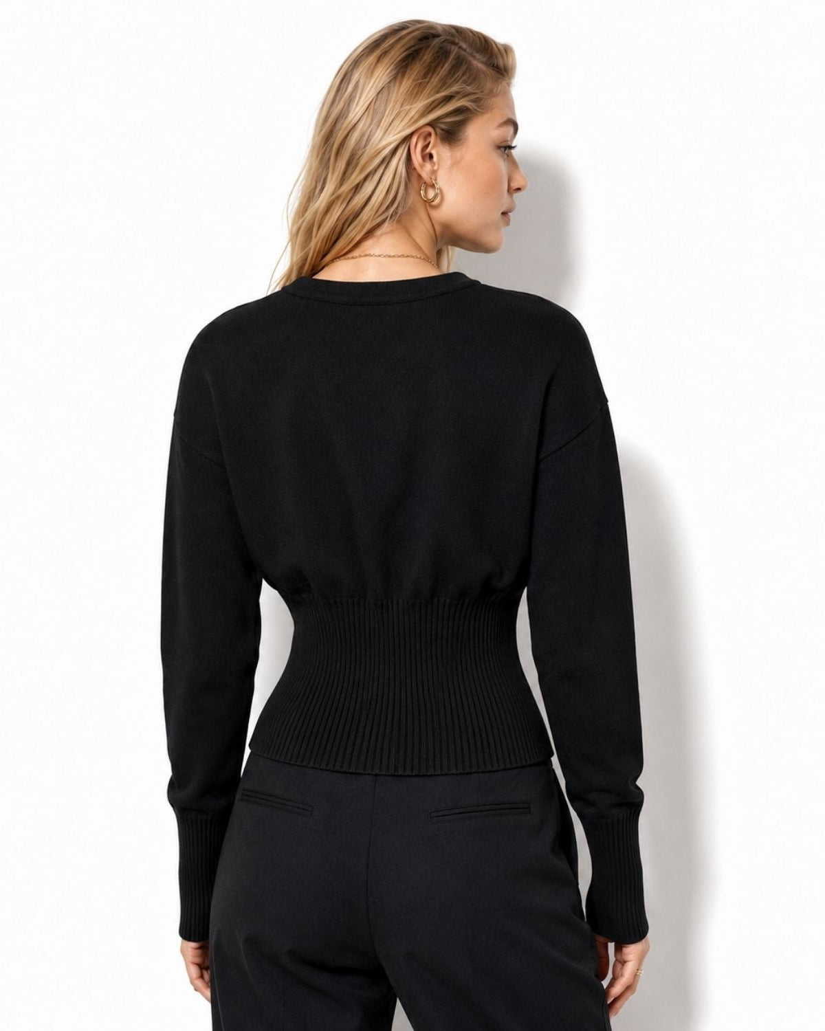 A woman shown from the back wearing a fitted black long-sleeve knit top with a ribbed waistband, paired with black pants, against a plain white studio background.