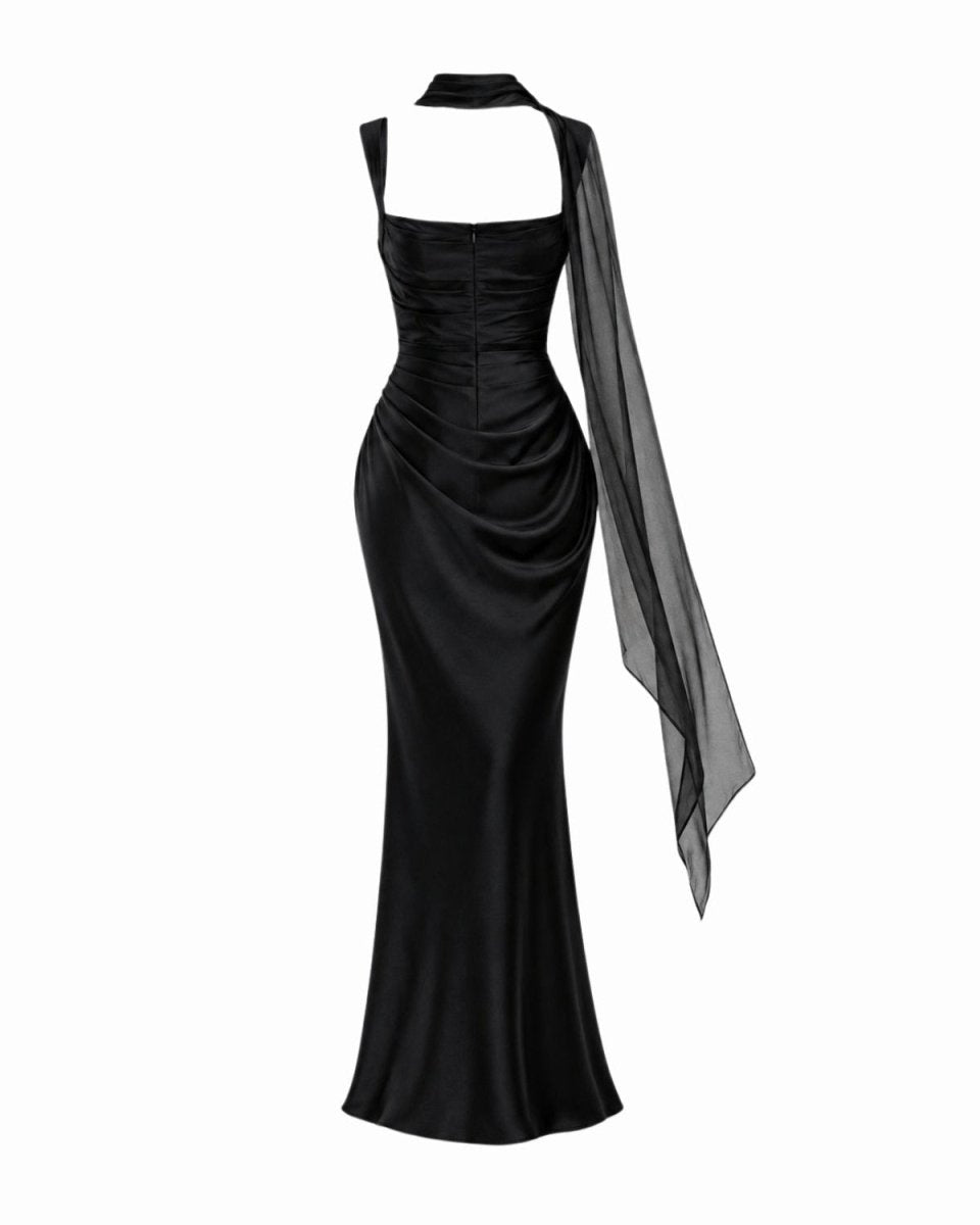 A black halter-neck floor-length gown with a structured corset-style bodice, draped skirt, and a sheer black asymmetrical draped overlay, shown on a white background.