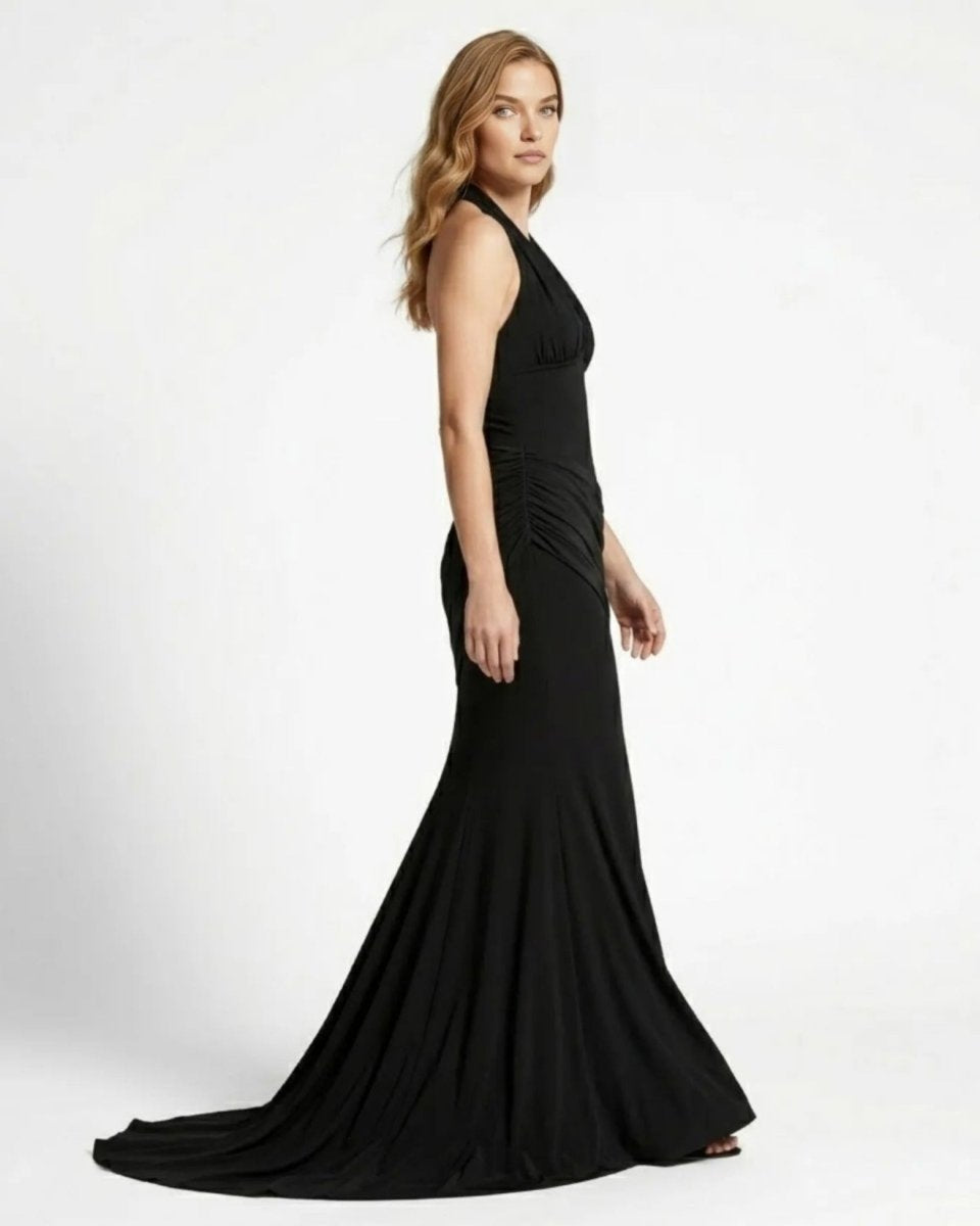 Side profile view of a glamorous black form-fitting mermaid evening gown highlighting asymmetrical draped hip details by Fenlo.
