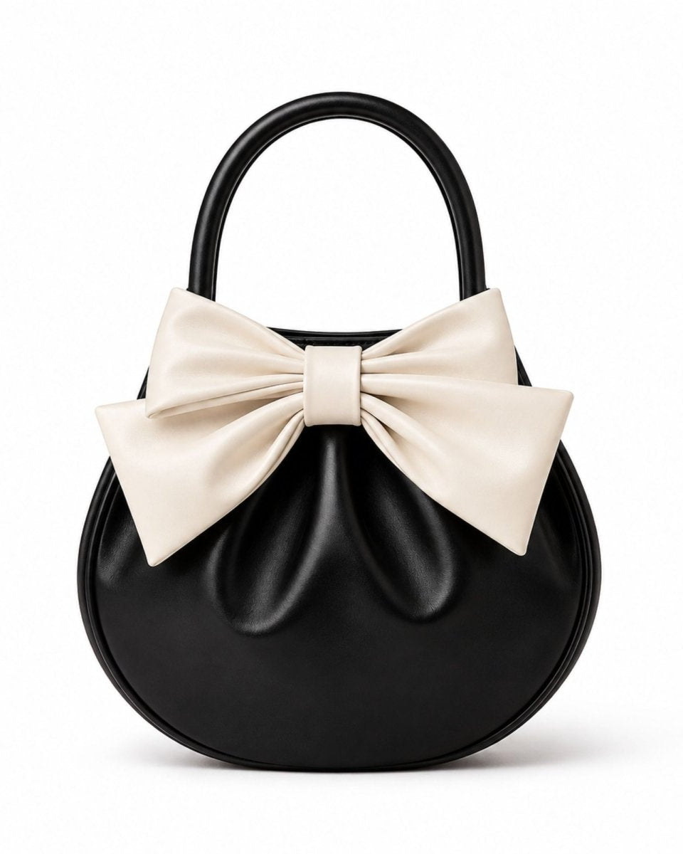 Front view of luxury round black leather handbag featuring an oversized cream statement bow and structured top handle against a white background.