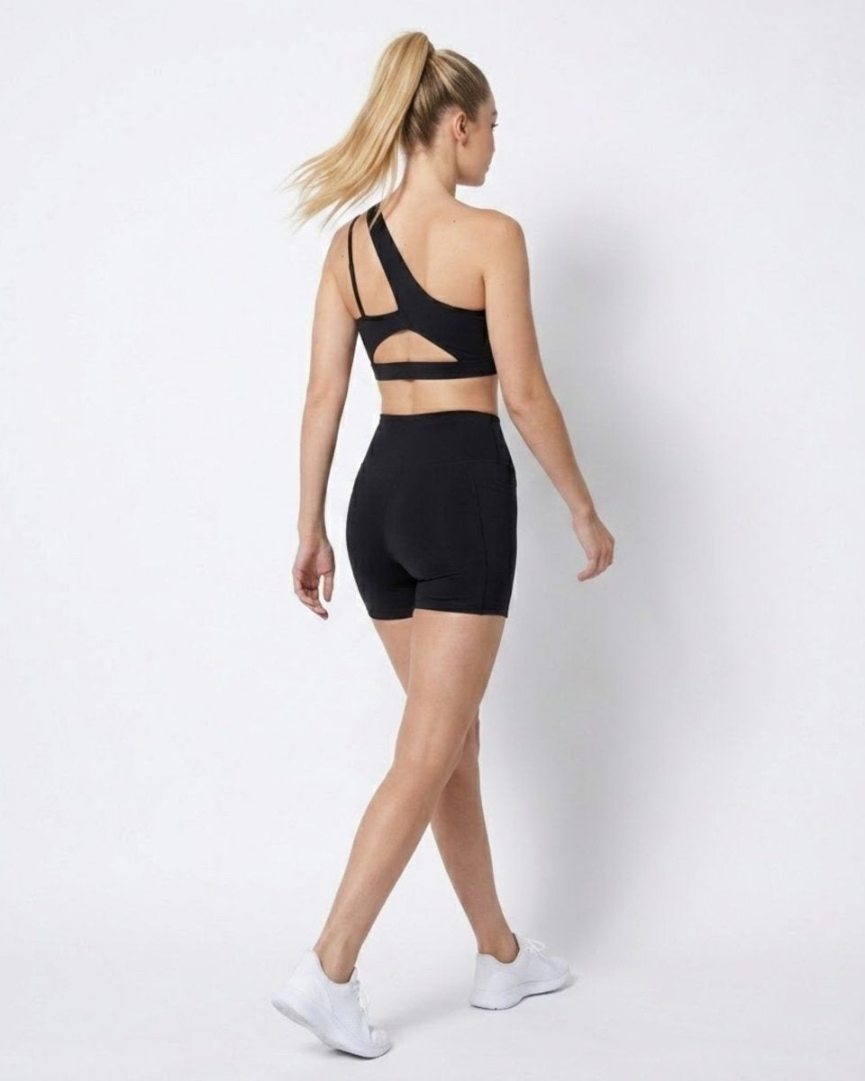 Back view of woman in black activewear set featuring an open strappy back sports bra and high waisted shorts 