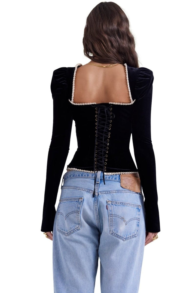 Person wearing a black kouvr long-sleeve top with cut-out design and light blue jeans on a white background