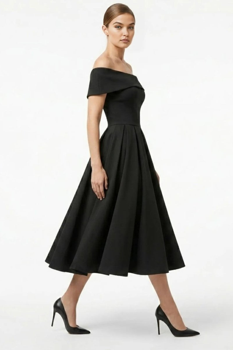 Side profile of a model wearing a fitted black vintage style cocktail dress showcasing the sweeping pleated skirt