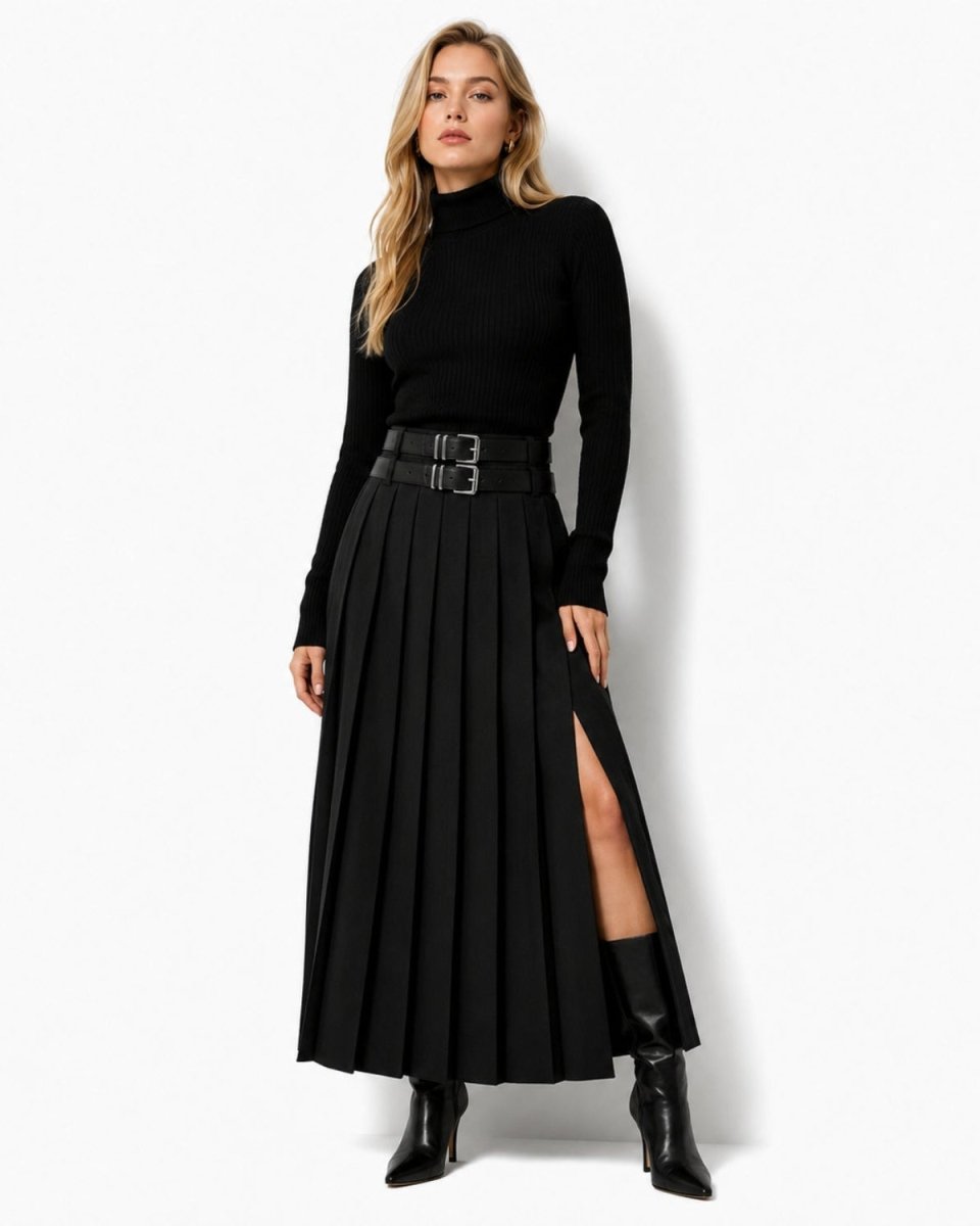 A woman modeling a black long-sleeve mock-neck top paired with a high-waisted black pleated midi skirt featuring a wide double-buckle belt and a thigh-high slit, styled with black ankle boots against a plain white studio background.