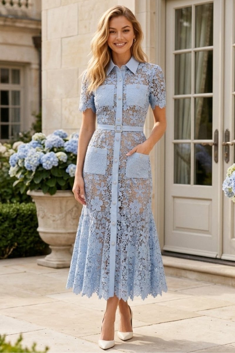 A woman models a light blue lace midi dress with short sleeves, a button-up front, and patch pockets, standing outdoors in front of a stone building with white doors and blue hydrangeas.