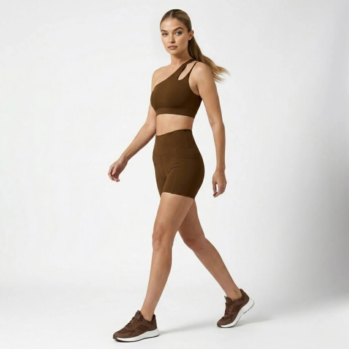 Profile view of woman walking in brown asymmetrical matching gym outfit with side pockets