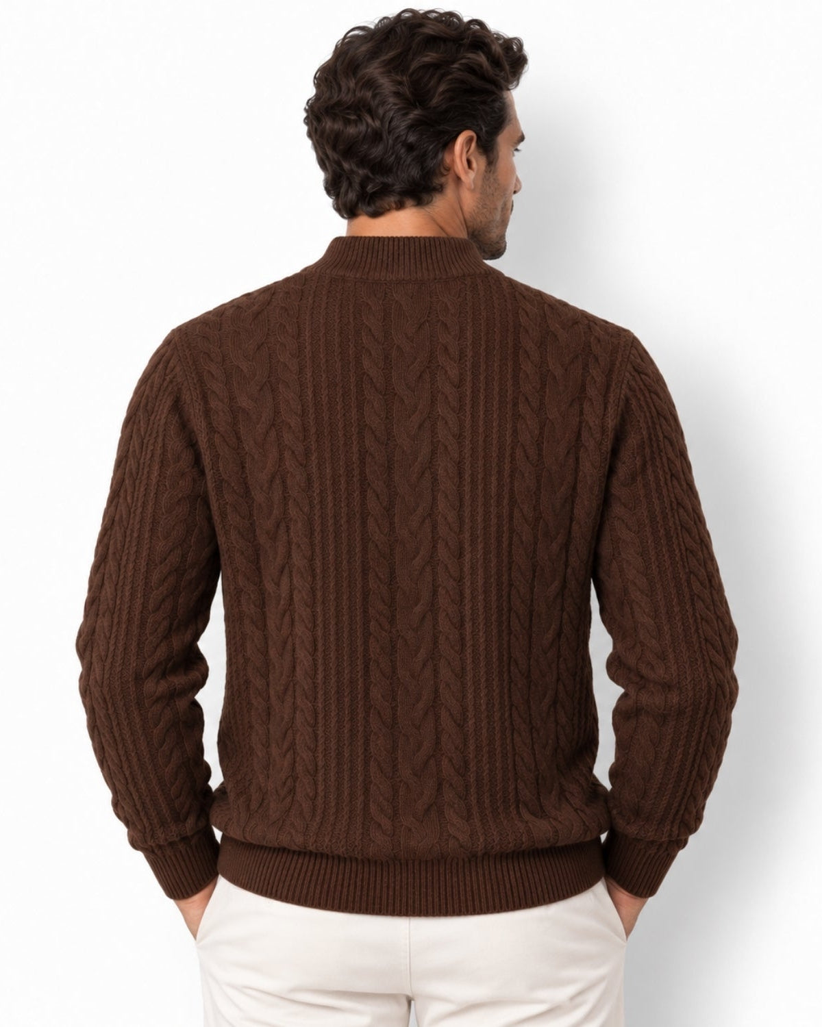 A man viewed from the back wearing a dark brown cable-knit sweater and white pants, standing against a plain white studio background.