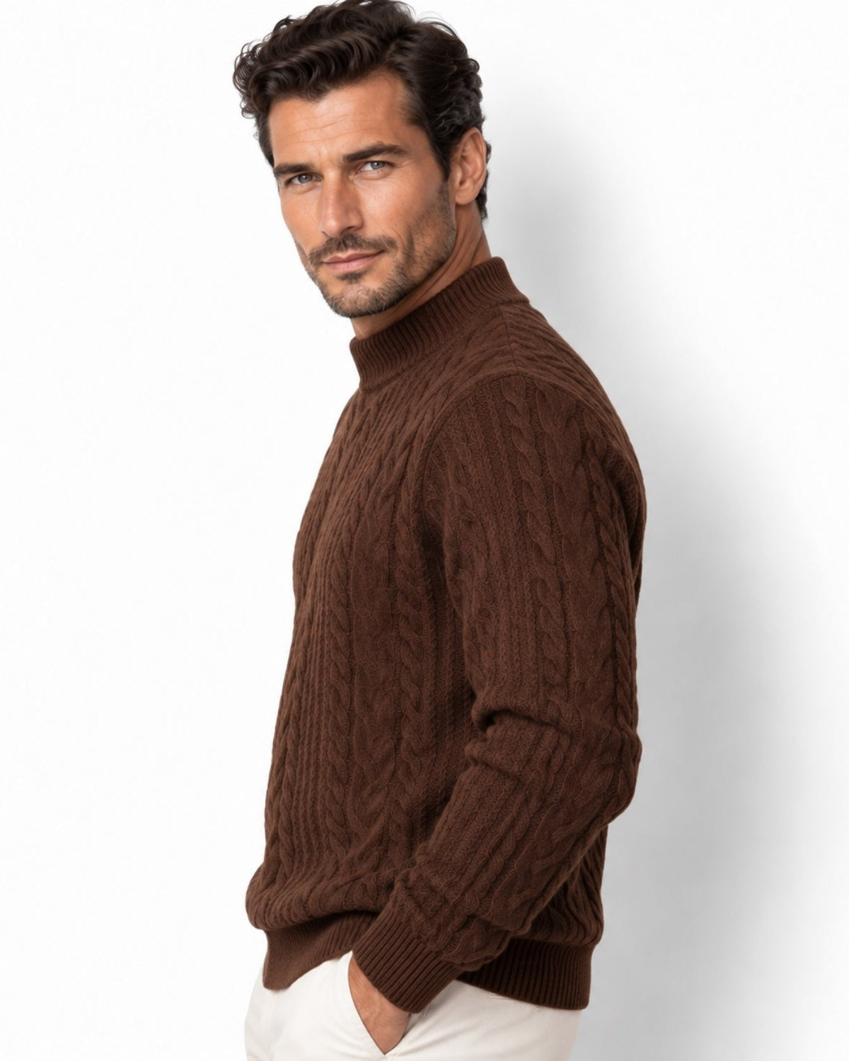 A man wearing a brown cable-knit mock neck sweater and white trousers, photographed against a clean white studio background.