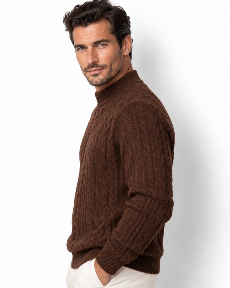 A man wearing a brown cable-knit mock neck sweater and white trousers, photographed against a clean white studio background.