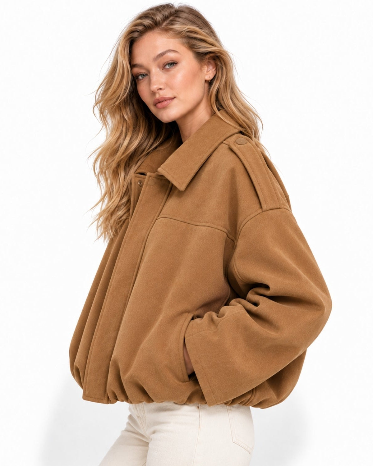 A woman wearing a cropped, oversized camel-brown suede jacket and white pants, photographed against a clean white studio background.
