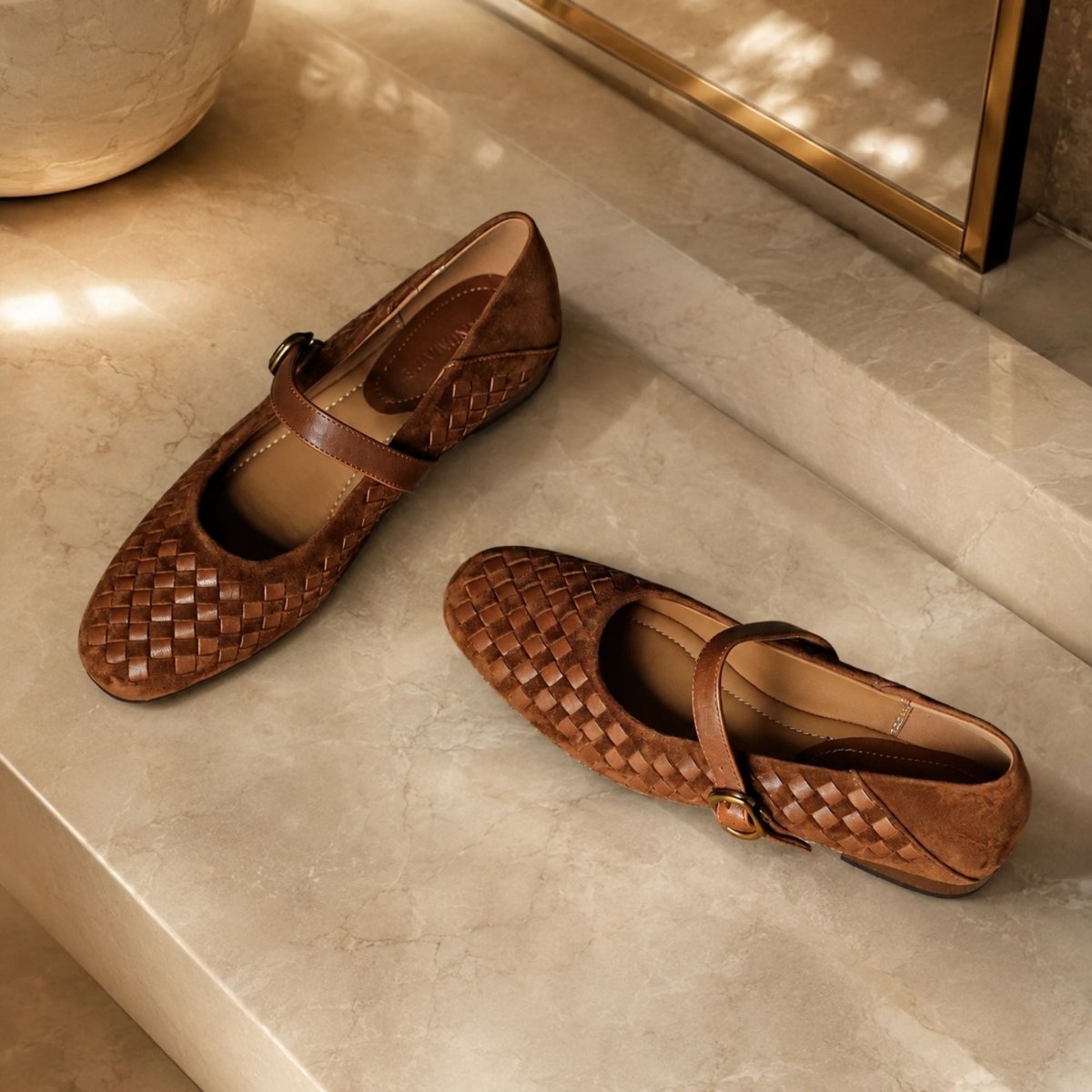 A pair of brown woven leather Mary Jane flats with strap buckles, styled on a beige marble surface.