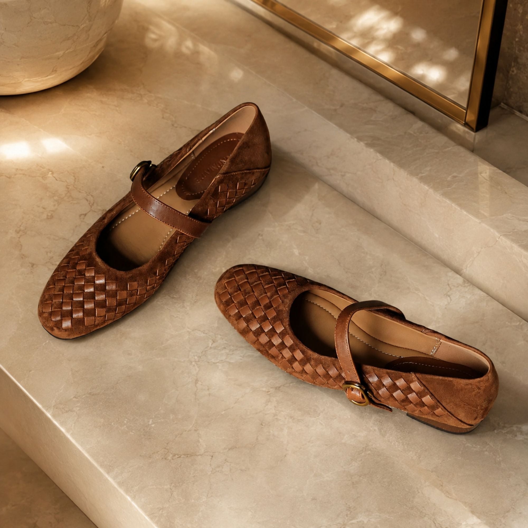 A pair of brown woven leather Mary Jane flats with strap buckles, styled on a beige marble surface.