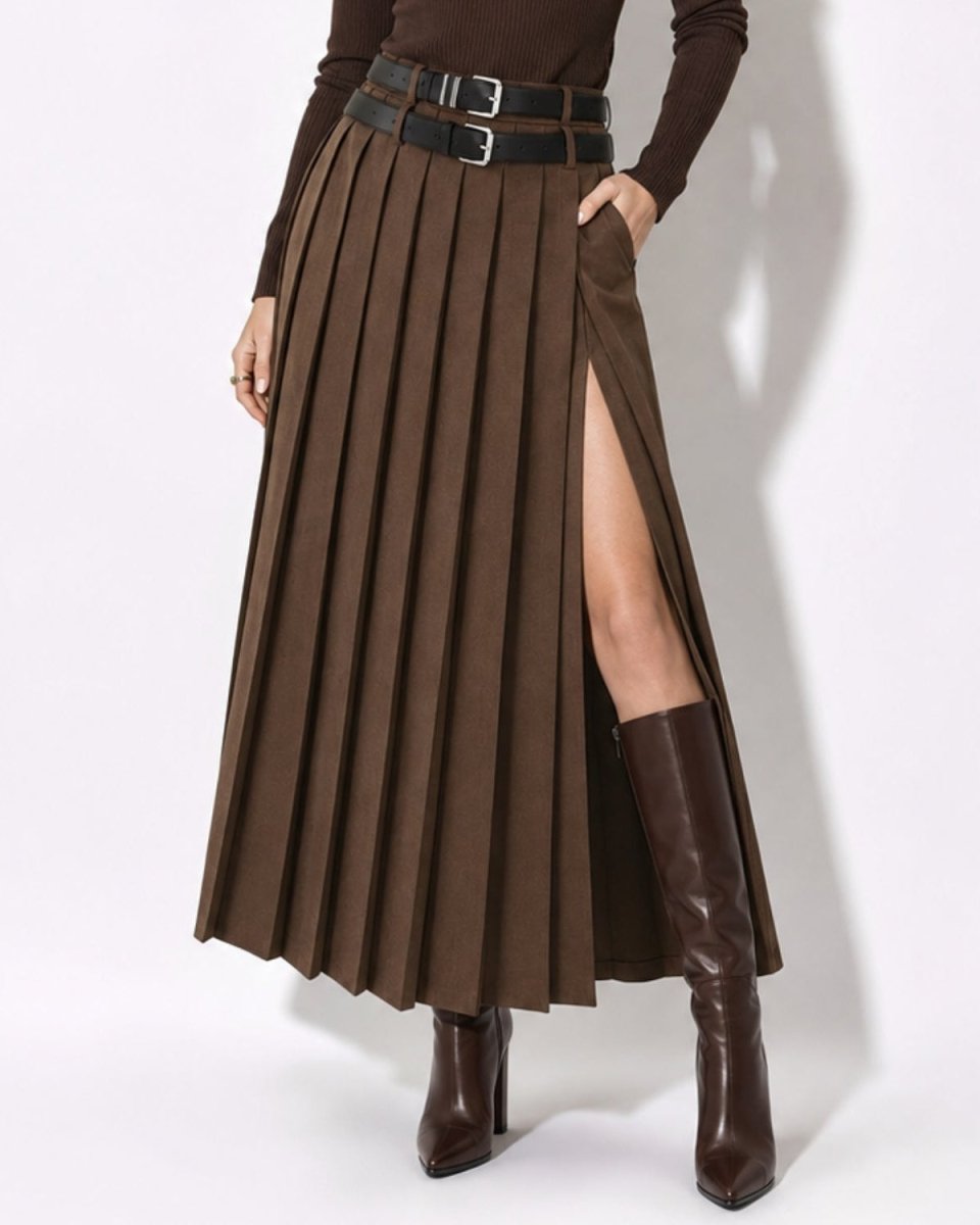 A model wearing a brown pleated maxi skirt with a high side slit, styled with a double black belt, a dark brown long-sleeve top, and dark brown knee-high boots against a white studio background.