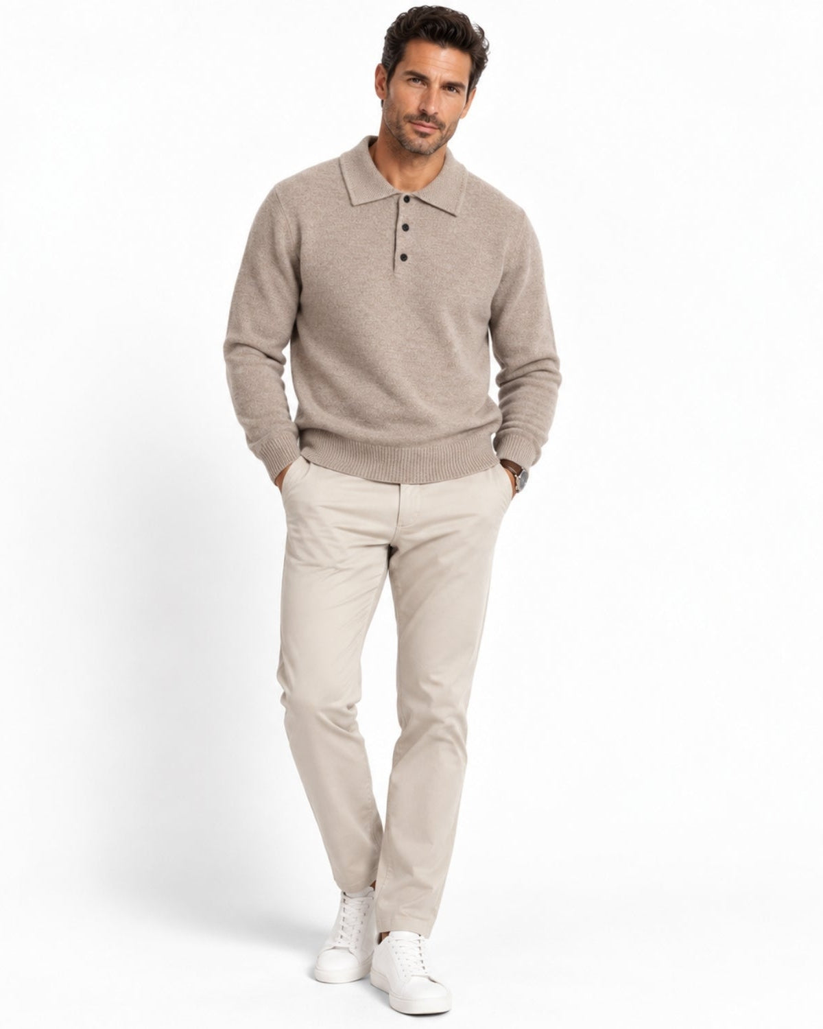 A man modeling a light taupe knit polo sweater and beige trousers with white sneakers, standing against a clean white studio background.