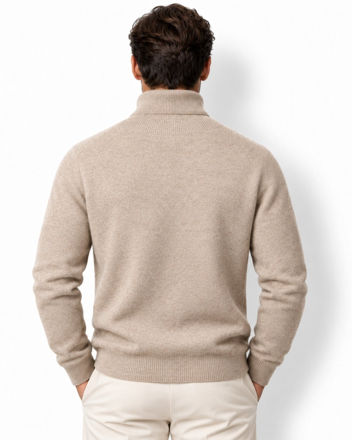 A man viewed from behind wearing a light camel knit mock neck sweater and cream trousers, standing against a plain white background.