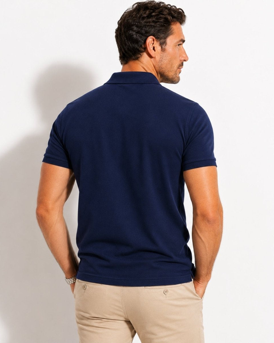 Man wearing a navy blue polo shirt and beige pants against a white background