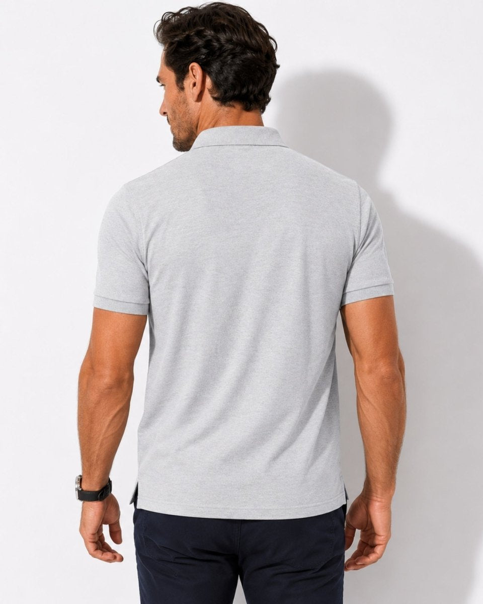 Man wearing a gray polo shirt and dark pants against a white background