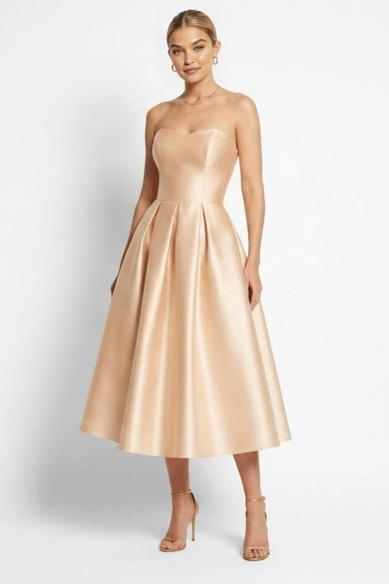 Woman wearing Fenlo Form champagne satin strapless pleated midi dress with sweetheart neckline facing forward