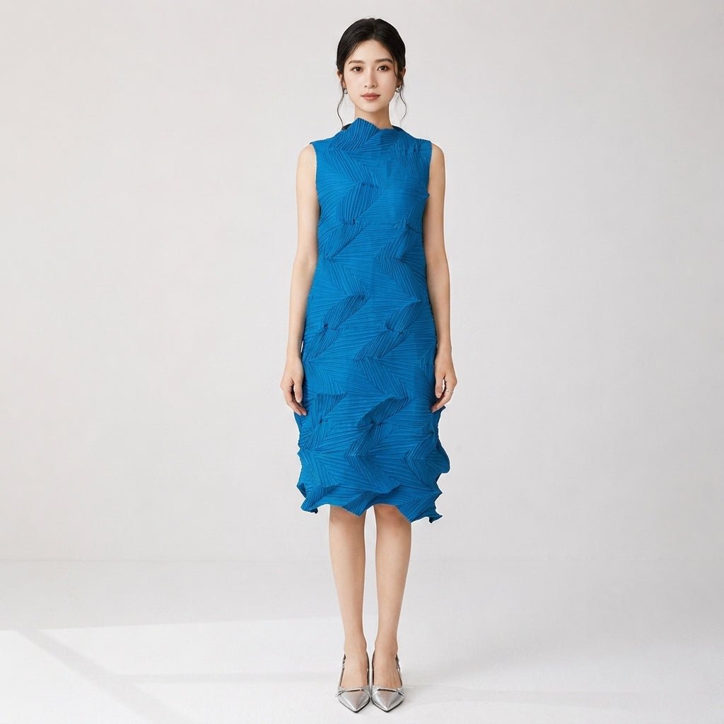 Front view of Asian female model wearing cobalt blue architectural pleated sleeveless midi dress with silver heels in a studio setting.