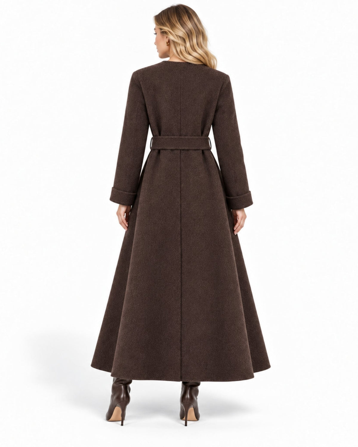 A woman viewed from the back wearing a long brown belted coat and brown pointed-toe heeled boots against a clean white studio background.