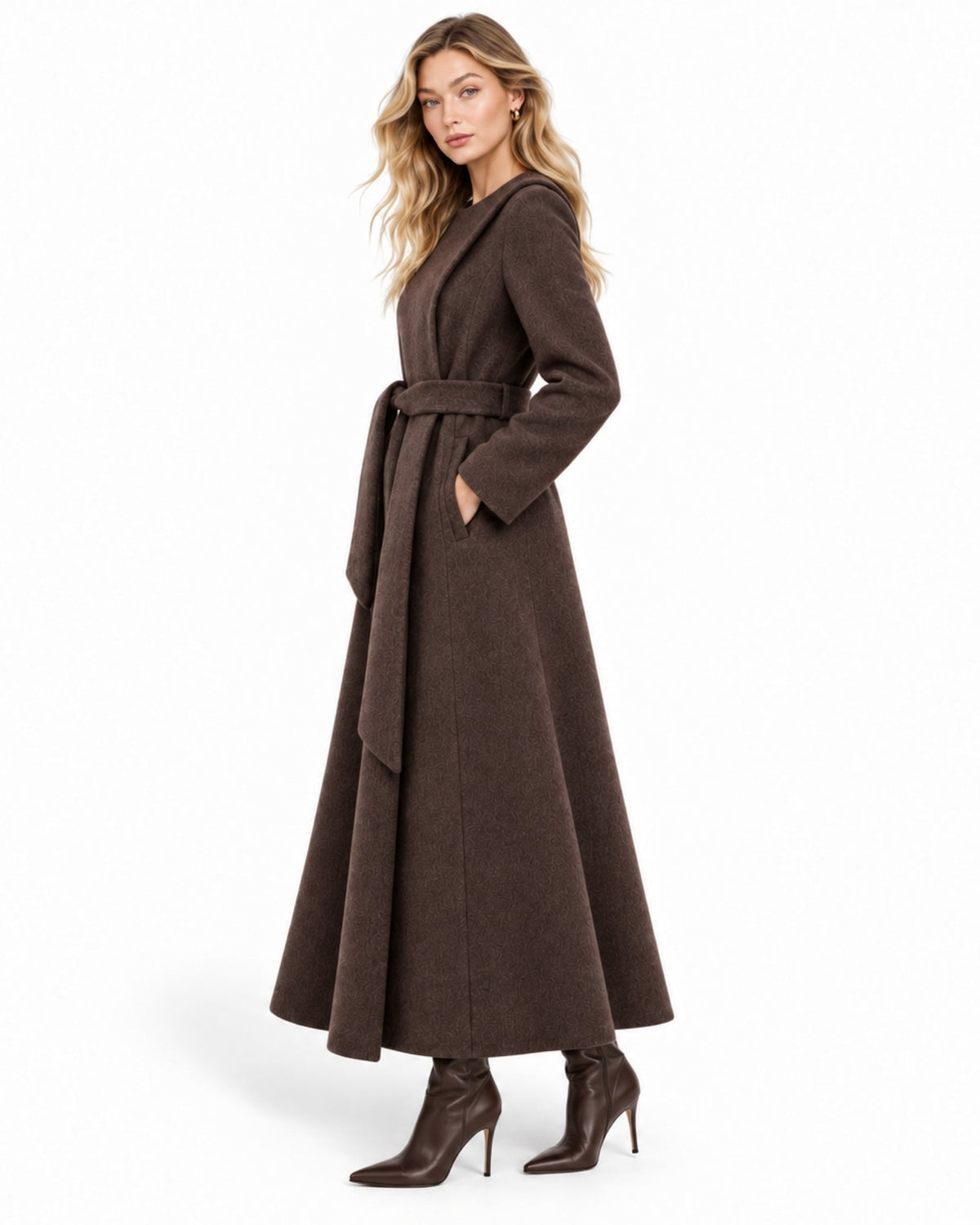 A woman modeling a long, dark brown belted coat with a draped collar, paired with dark brown heeled ankle boots, against a plain white studio background.