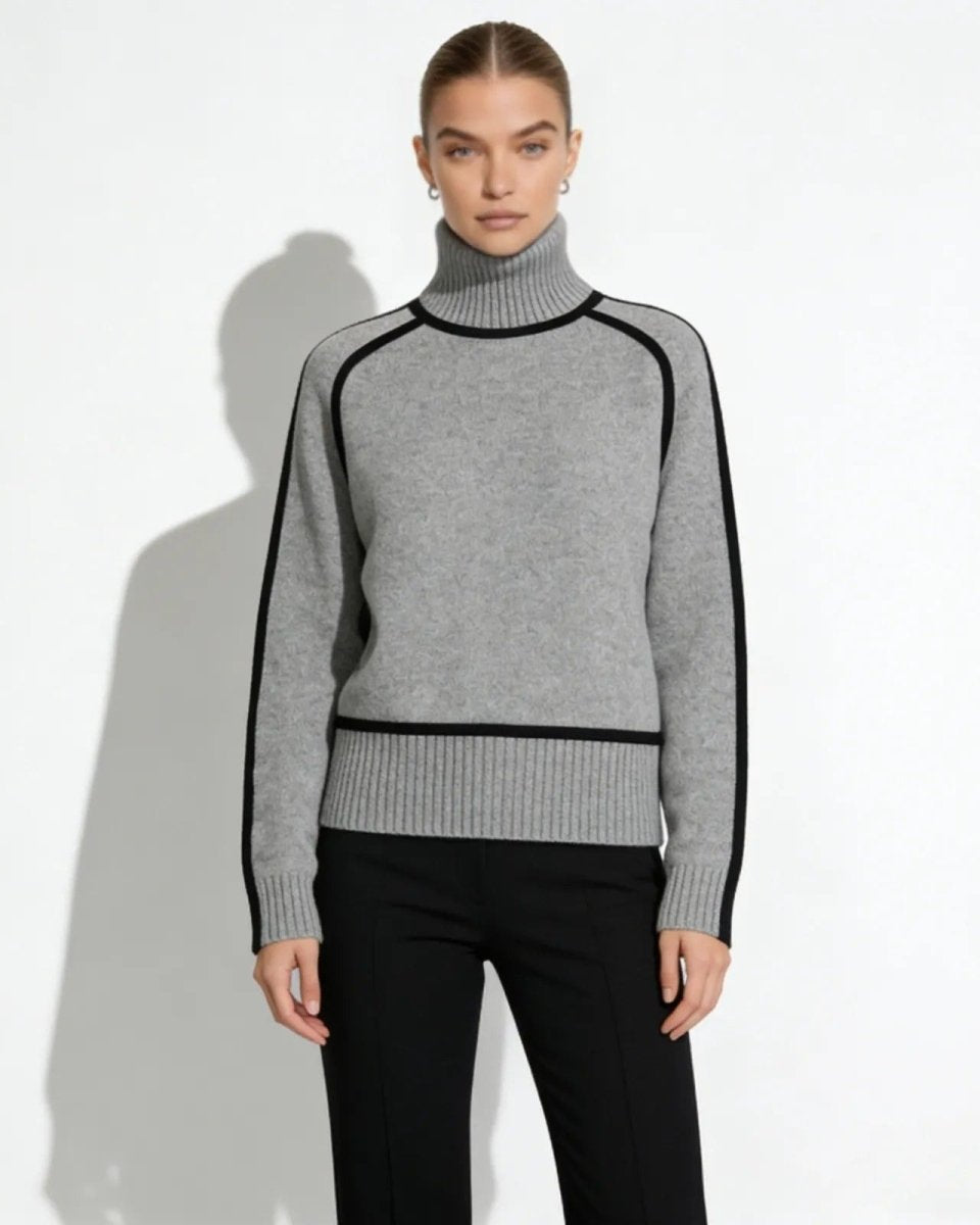 Model wearing gray cashmere turtleneck sweater with black piping detail, front view.