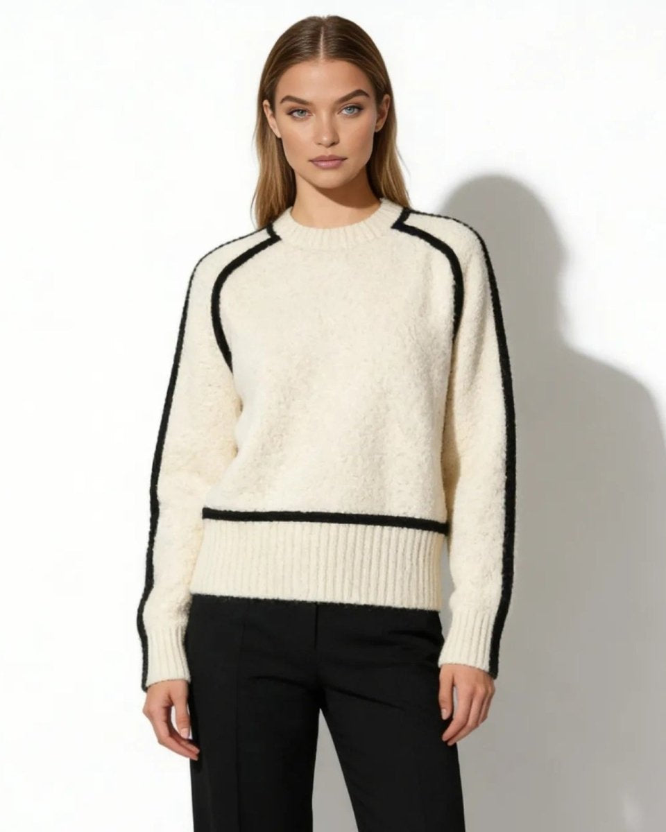 Model wearing white wool turtleneck sweater with black contrast trim on sleeves and hem, paired with black trousers.