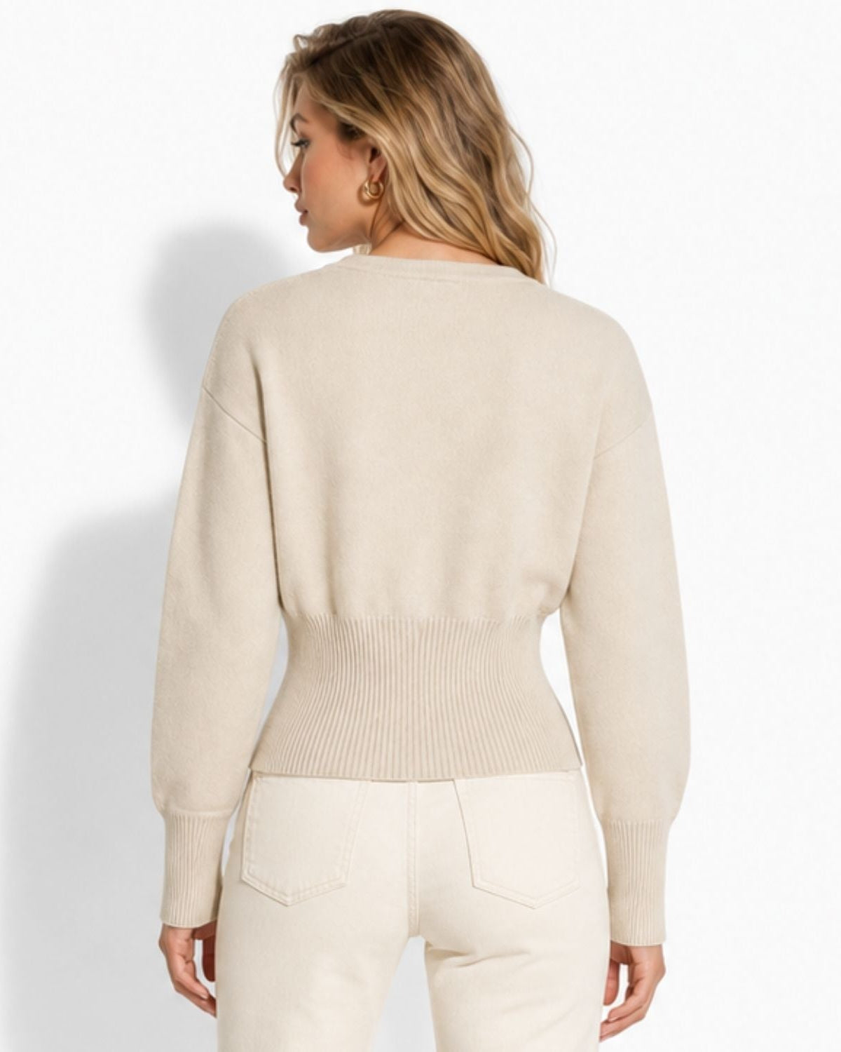 A woman shown from the back wearing a light beige knit sweater and cream pants against a plain white studio background.