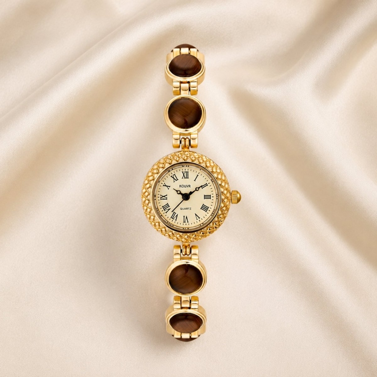 Flat lay view of a dainty gold jewelry watch for women, highlighting the quilted lattice bezel, classic roman numeral dial, and smooth tiger's eye stone bracelet links on silk.