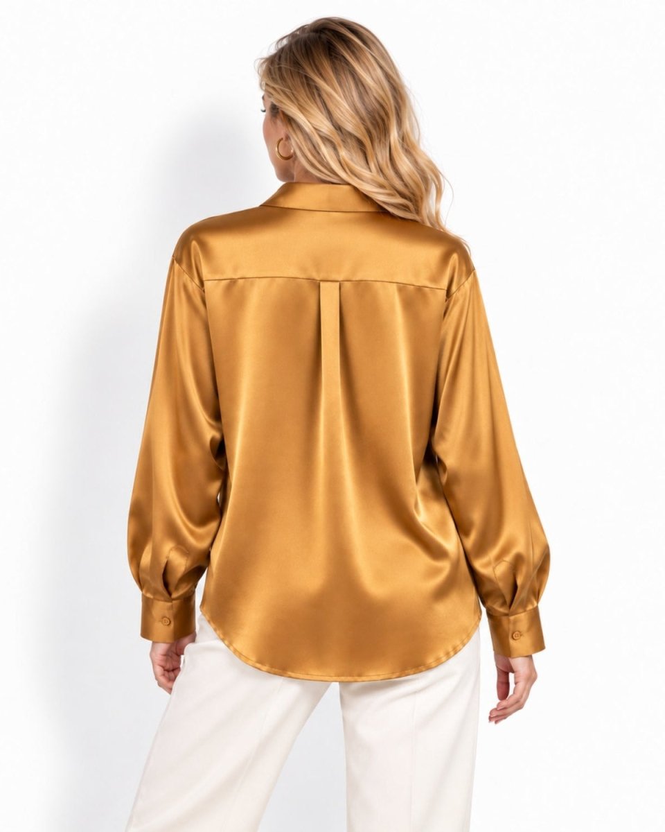 A woman viewed from the back wearing a shiny gold silk button-up blouse and white pants, photographed against a clean white studio background.
