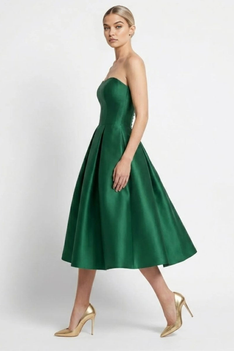Side profile of a blonde fashion model walking in a formal green fit and flare cocktail dress paired with gold stiletto heels.