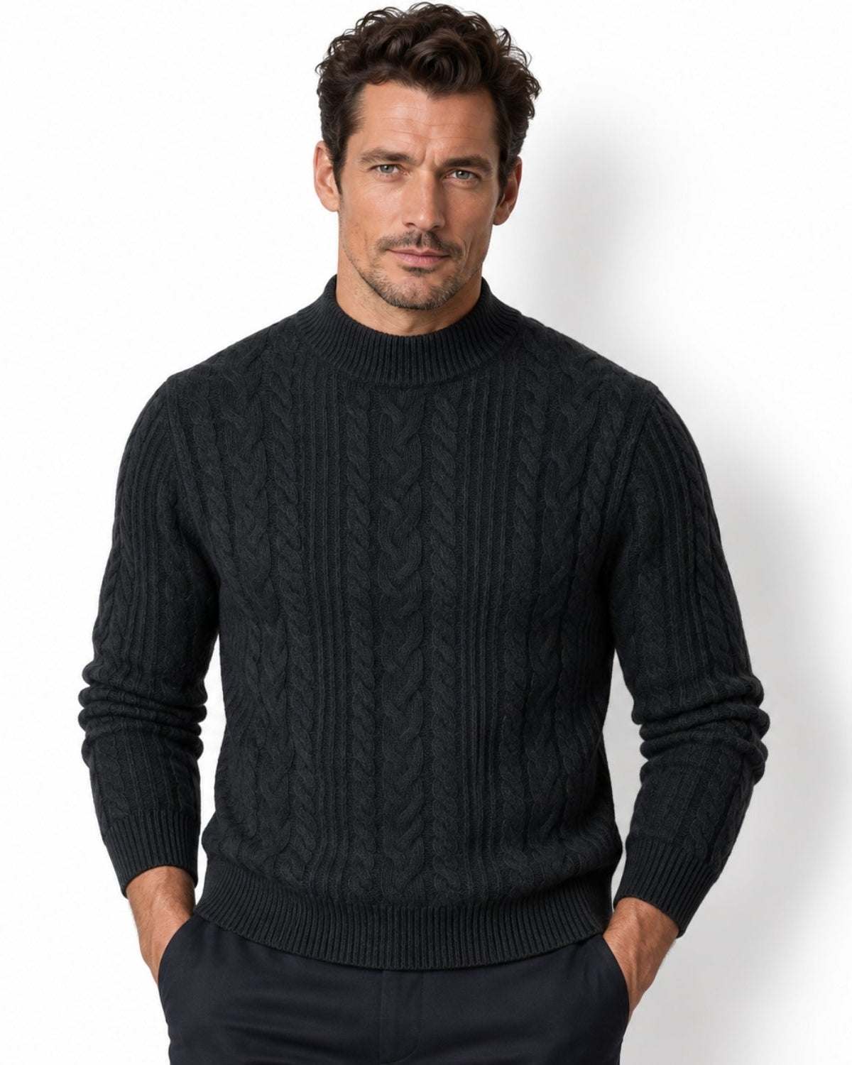 Front view of a man wearing a luxury dark grey cable knit mock neck sweater, hands in pockets, demonstrating a classic tailored fit.